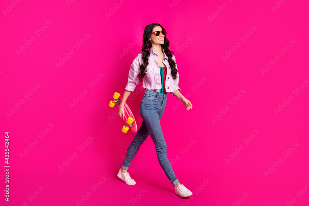 Full size profile side photo of young beautiful cool confident girl go walk with skateboard isolated on pink color background Full size profile side photo of young beautiful cool confident girl go walk with skateboard isolated on pink color background