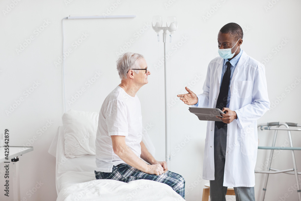Side view portrait of African-American doctor talking to senior patient in white hospital room, copy space