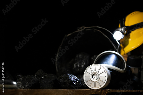 On black coal folded mining accessories: yellow helmet with flashlight, dust mask with filter