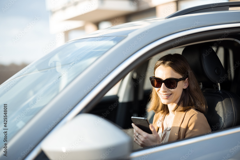 Naklejka premium Young woman in sunglasses talking on the phone and driving a car. Businesswoman going to work from the house.