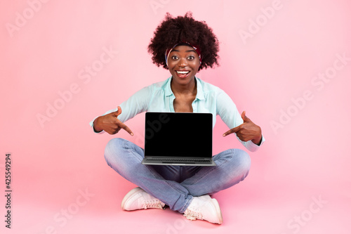 Black Young Woman Showing Laptop Empty Screen Sitting, Pink Background © Prostock-studio