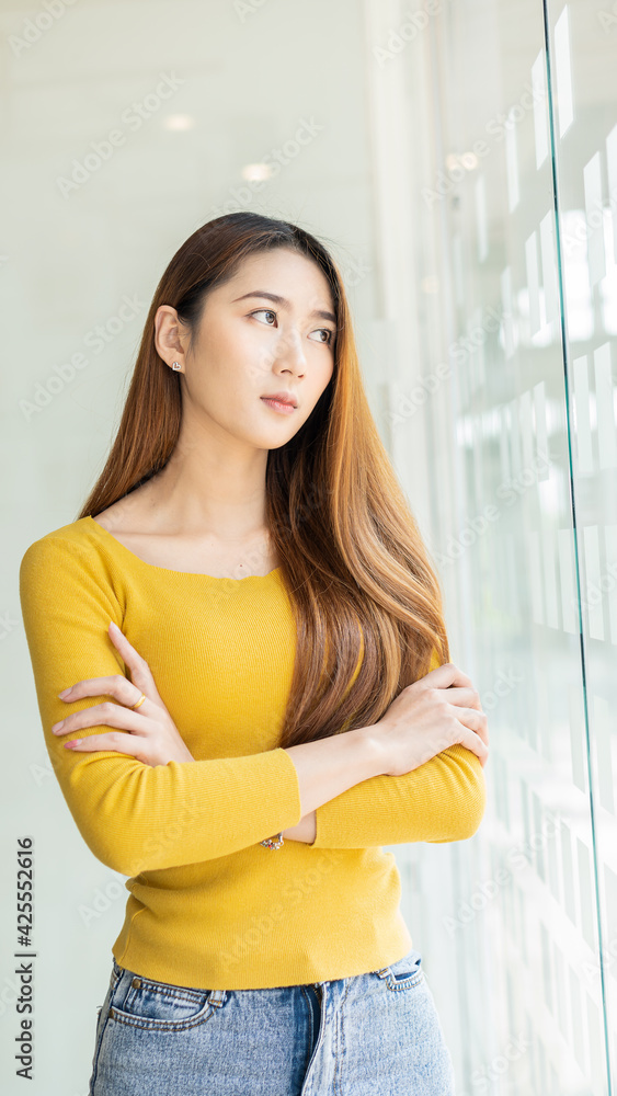 An Asian female student stands by a glass wall in a coffee shop.