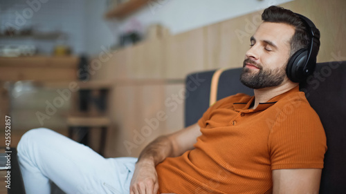 pleased man in wireless headphones chilling in cafe