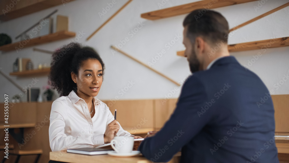 Fototapeta premium interracial business partners talking during meeting in cafe