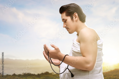 Asian Muslim man in ihram clothes praying with prayer beads on his hands
