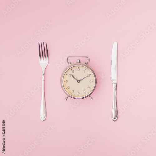 Old clock, knife and fork on pink background. Minimal composition. Copy space.