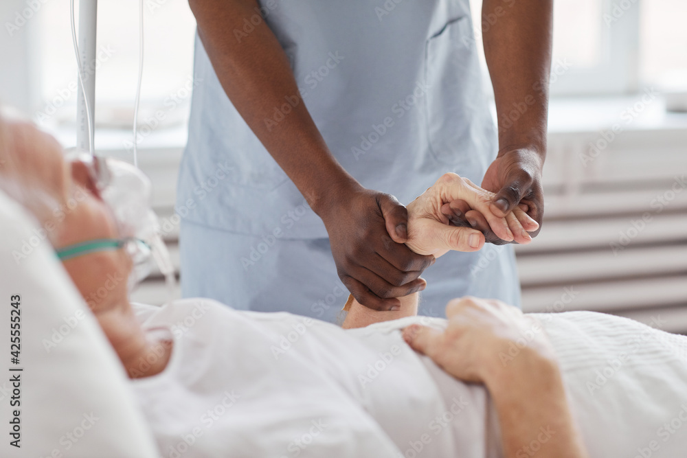 Obraz premium Close up of African-American male nurse holding hand of senior man in hospital and comforting him, copy space