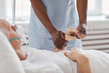Close up of African-American male nurse holding hand of senior man in hospital and comforting him, copy space