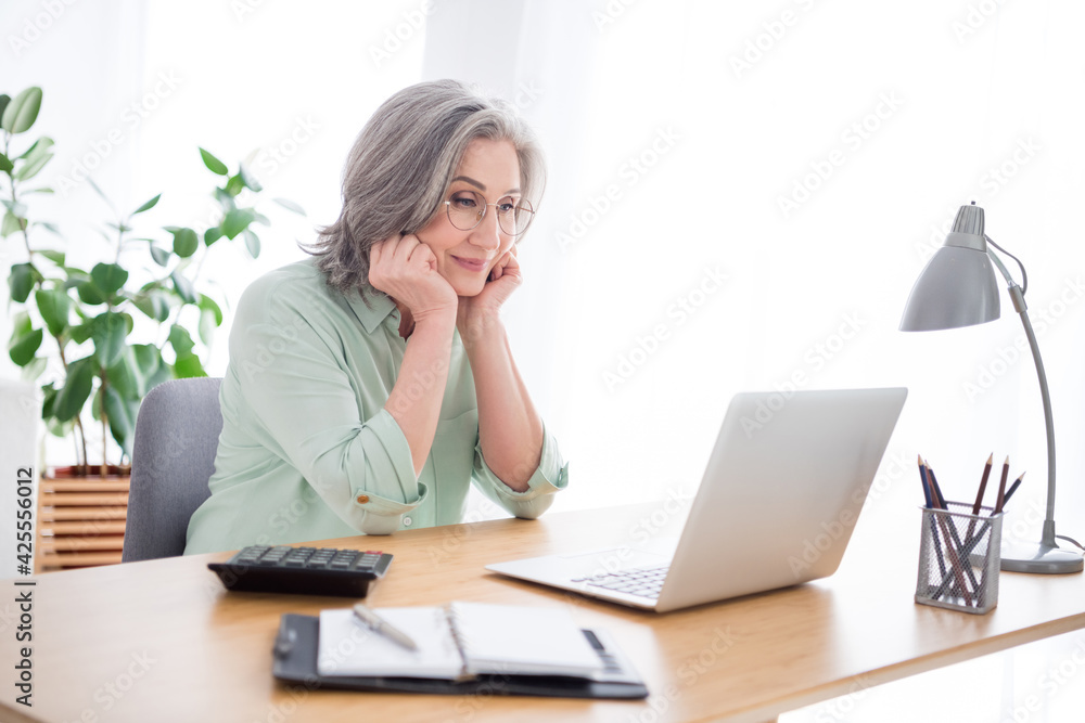 Profile photo of charming person sitting behind desk hands on cheeks look laptop enjoy working from home indoors Profile photo of charming person sitting behind desk hands on cheeks look laptop enjoy working from home indoors