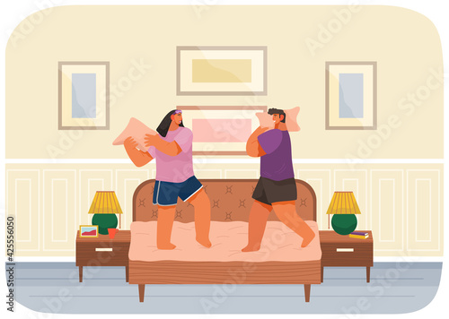 Young happy couple having pillow battle, man and woman wearing pajamas enjoying time together