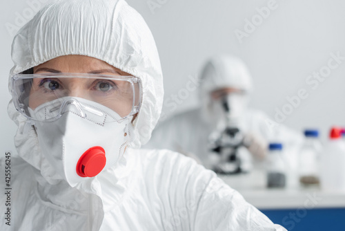 Scientist in goggles and hazmat suit looking at camera in laboratory