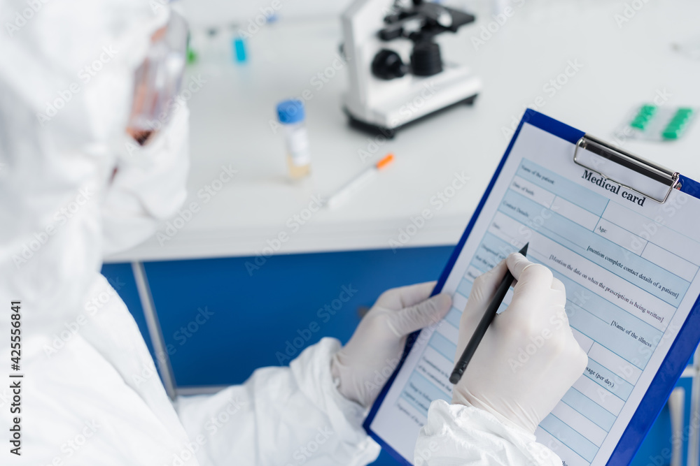 Medical card and pen in hands of scientist in protective uniform on blurred foreground Medical card and pen in hands of scientist in protective uniform on blurred foreground