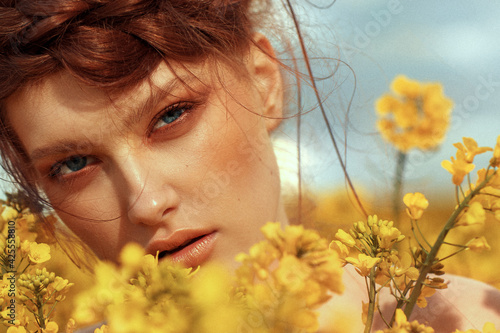  Young fashion model portrait with ginger hair and blue eyes in yellow rapeseed field
