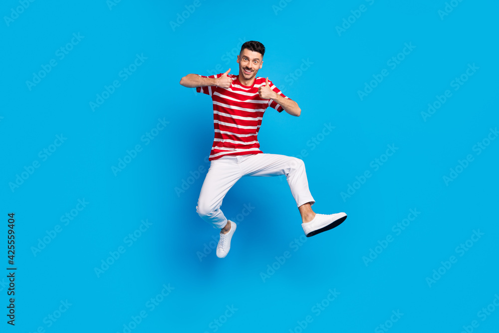 Full body photo of happy brunette positive young man show thumbs-up jump air isolated on blue color background