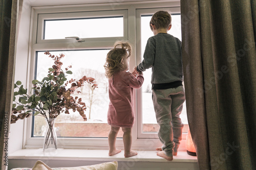 Happy children standing on the windowsill, looking through the window. Little girl and boy.