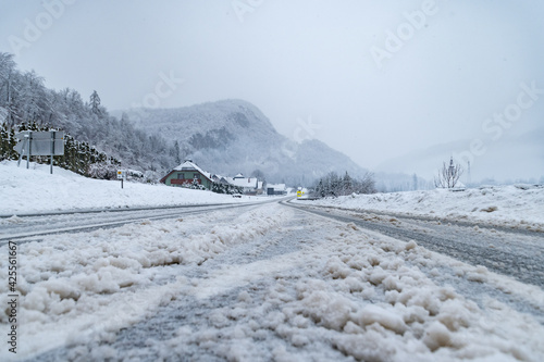 Low angle view of snowy countryside road in winter. Snowstorm in cold and cloudy weather. Small village in Alpine valley, Slovenia