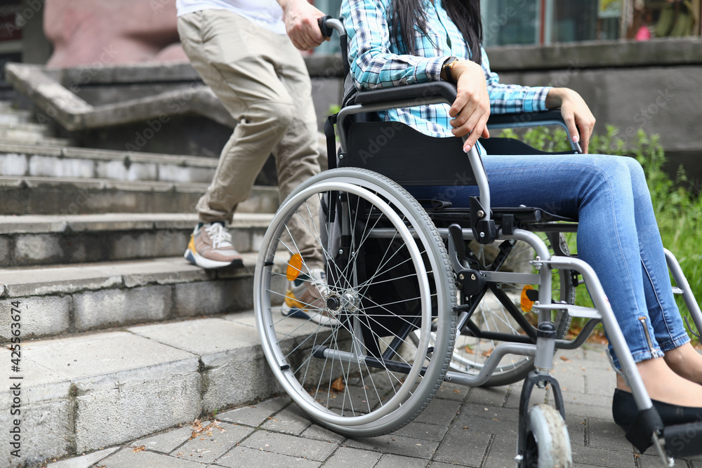 Obraz premium Man tries to drag wheelchair with woman onto stairs