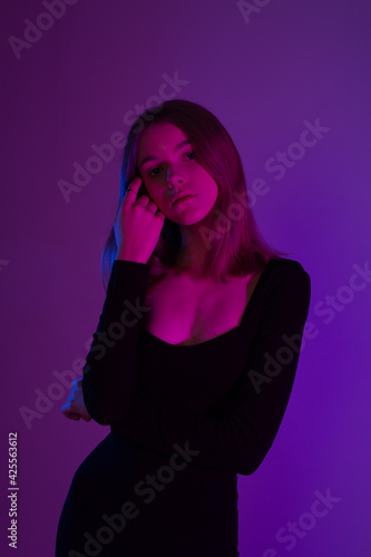 Girl portrait in neon light. Young slim woman model in black dress