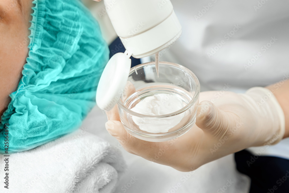 The beautician is putting cream on the face mask. The concept of facial hygiene, cosmetic procedures, skin care, skin pore cleansing, SPA, hardware cosmetology. The beautician is putting cream on the face mask. The concept of facial hygiene, cosmetic procedures, skin care, skin pore cleansing, SPA, hardware cosmetology.