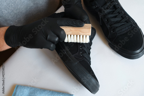 Man is cleaning sneakers in a workshop. Shoe shine service. The shoemaker prepares the shoes for the season. Shoe brush close-up. Shoe care with a special product photo