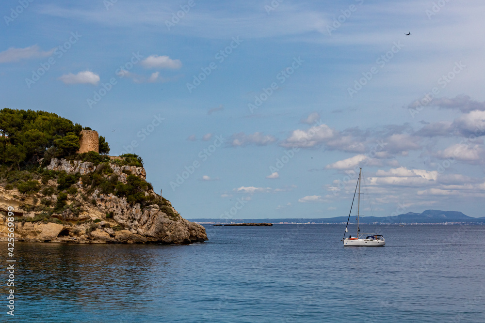 the coast of majorca from sea with ancient tower and sailboat in front in  spain