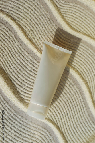 white cosmetic tube on a sand textured background with hard shadow