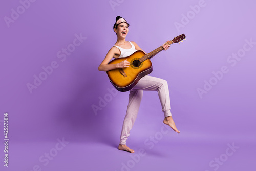 Full size photo of happy excited smiling funky girl in pajamas playing acoustic guitar isolated on violet color background