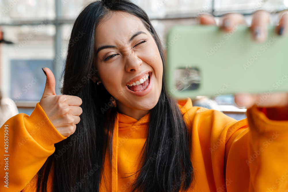 Smiling asian woman gesturing thumb up while taking selfie on cellphone Smiling asian woman gesturing thumb up while taking selfie on cellphone