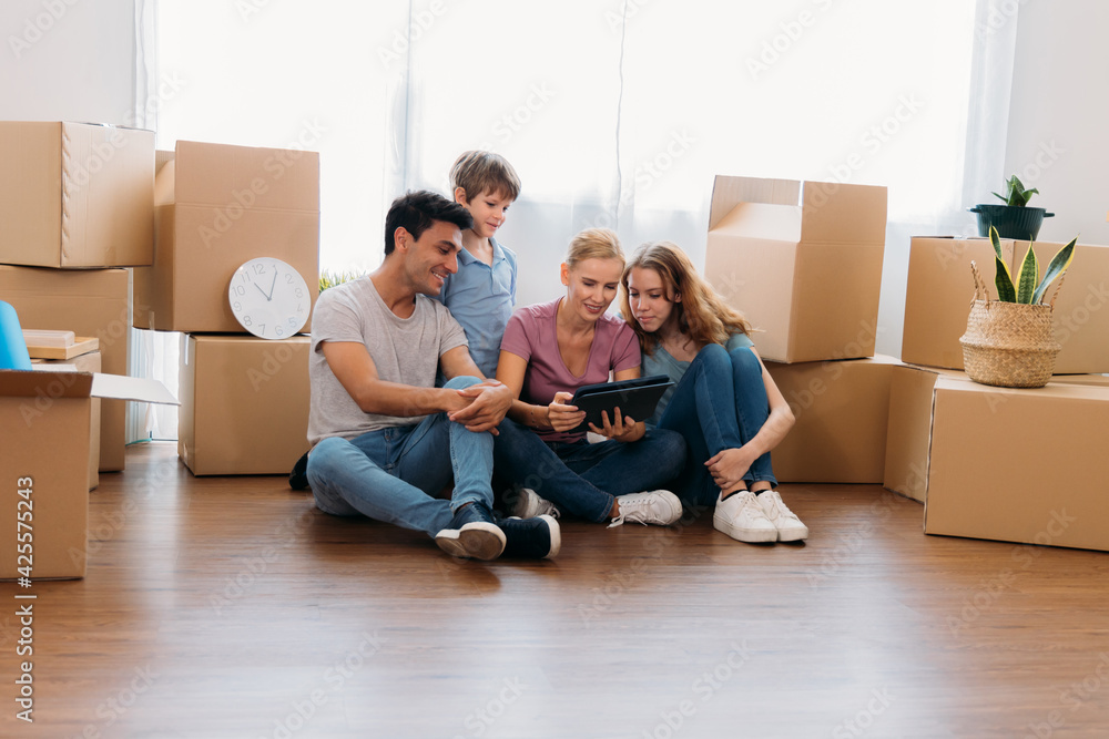 Cheerful and beautiful caucasian mother holding digital tablet and shopping for furniture for new home with handsome husband and children with cardboard boxes around Cheerful and beautiful caucasian mother holding digital tablet and shopping for furniture for new home with handsome husband and children with cardboard boxes around