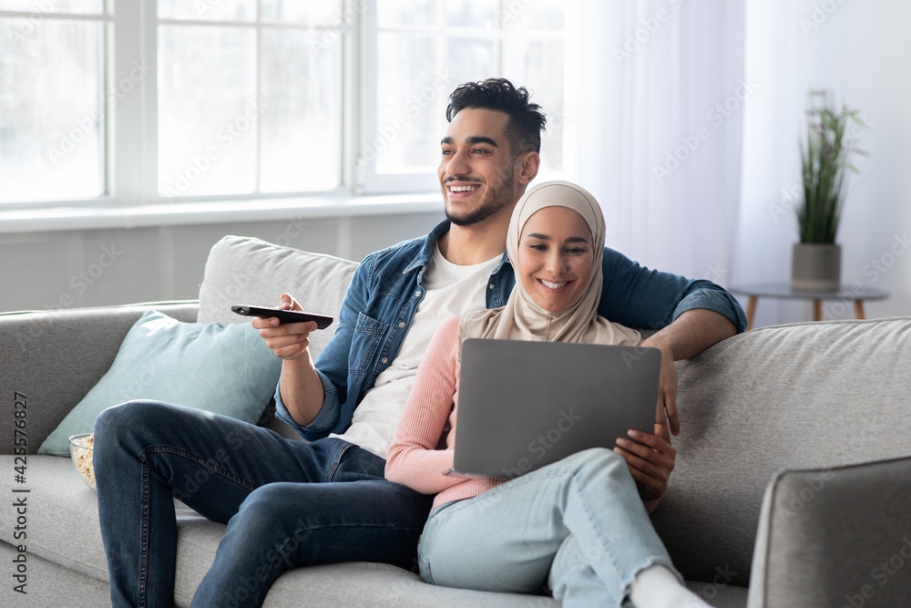 Happy arab man with remote hugging muslim woman with laptop Happy arab man with remote hugging muslim woman with laptop