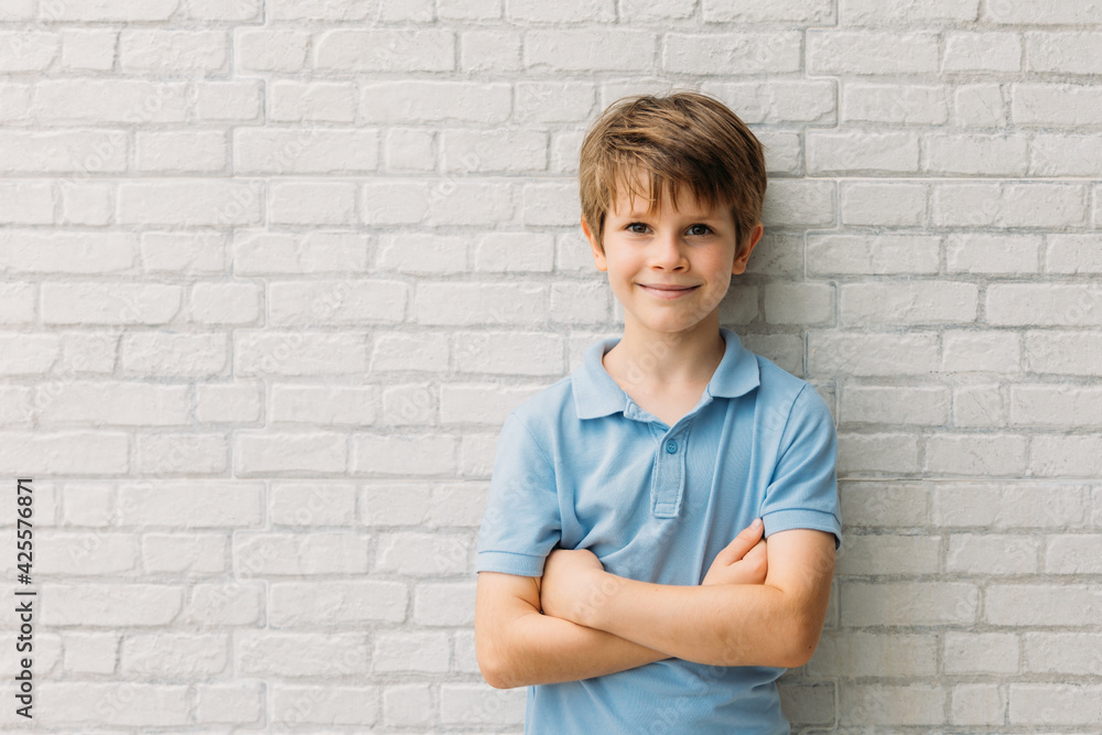 Portrait of happy young caucasian boy in casual outfit with arms crossed isolated over white bricks background smiling and looking at camera Portrait of happy young caucasian boy in casual outfit with arms crossed isolated over white bricks background smiling and looking at camera