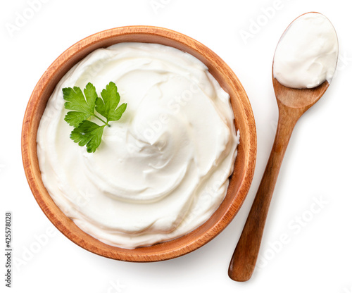 Fotografija Sour cream in a wooden plate and spoon on a white background, isolated