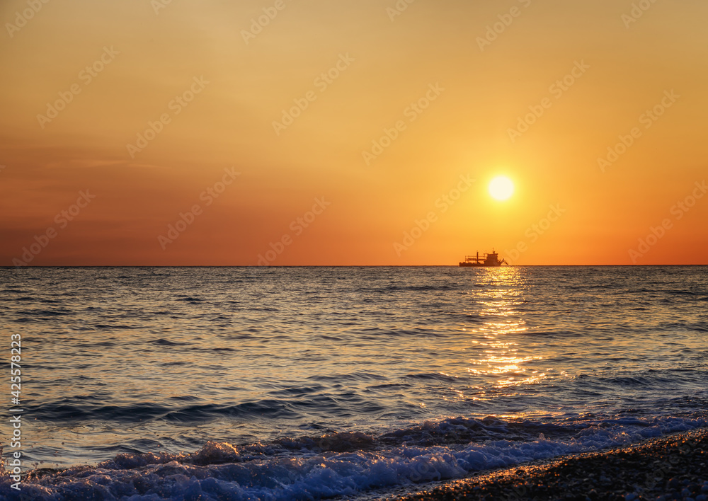 Golden sunset over the Black Sea (Adler, Russia) in summer. An enchanting picture with the sea sparkling from the sun on a summer evening. The disc of the sun is low above the surface of the water 