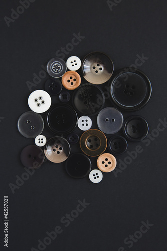 Many round buttons of different sizes on a black background, top view. Needlework and sewing concept. Handicraft.