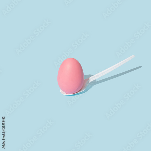 Pastel pink Easter egg on white plastic spoon. Trendy, creative and minimal spring concept.