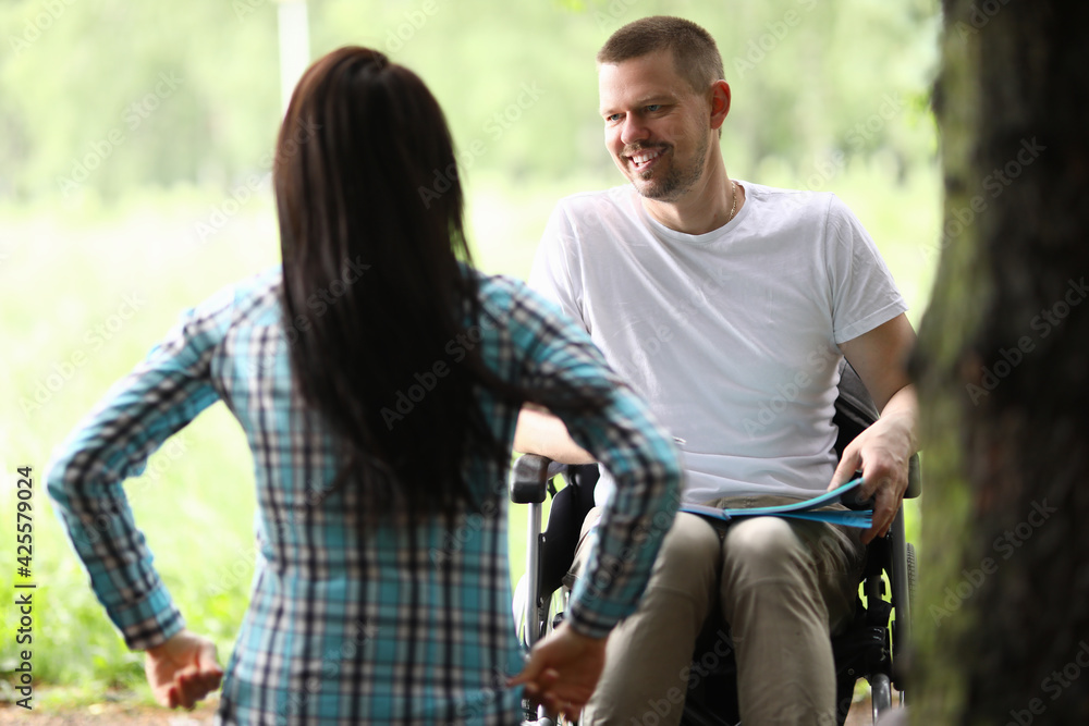 Man in wheelchair in park communicates with woman Man in wheelchair in park communicates with woman