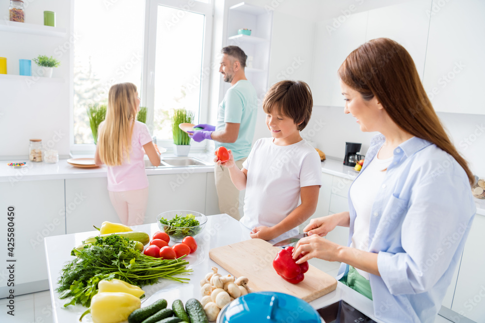 Photo of happy smiling positive lovely family cooking together little son helps mom with vegetables at home house Photo of happy smiling positive lovely family cooking together little son helps mom with vegetables at home house