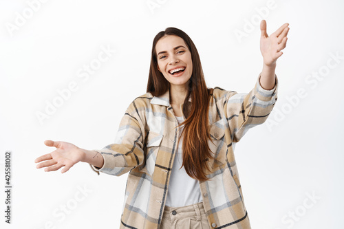 Beautiful smiling woman inviting you come closer, beckon for hug, extend hands and welcoming into her arms, embracing and greeting friends, standing over white background