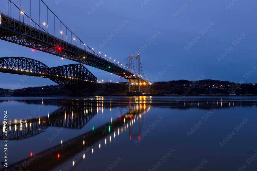 Low angle view of the 1970 suspension Pierre-Laporte Bridge and 1919 steel truss Quebec Bridge over the St. Lawrence River seen during a blue hour early morning, Quebec City, Quebec, Canada