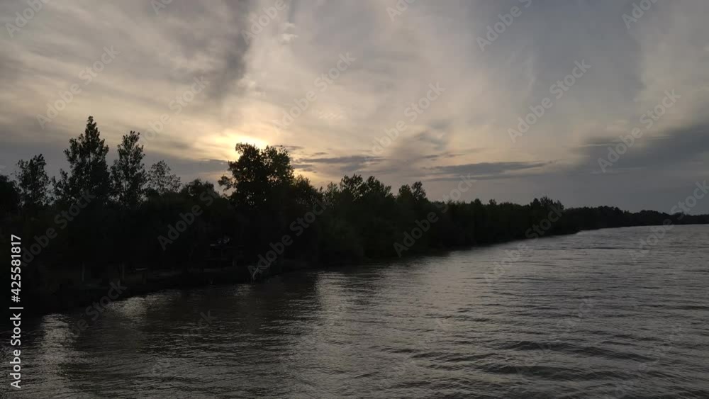 Aerial flyover cloudy sunset at river with sun behind trees Aerial flyover cloudy sunset at river with sun behind trees