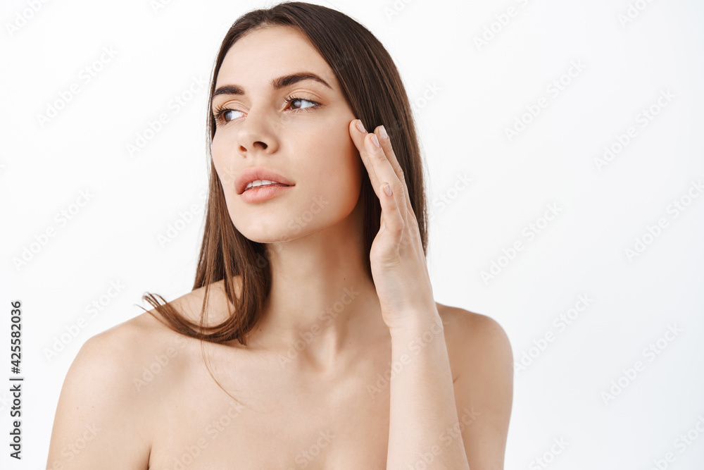 Portrait of young and beautiful woman with perfect smooth skin. Female model touching under eye skin, apply anti-aging wrinkles cream, look away thoughtful, Concept of natural cosmetics and skincare Portrait of young and beautiful woman with perfect smooth skin. Female model touching under eye skin, apply anti-aging wrinkles cream, look away thoughtful, Concept of natural cosmetics and skincare