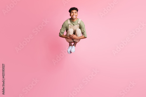 Photo of guy jump embrace knees beaming smile wear beige overall footwear isolated pink color background