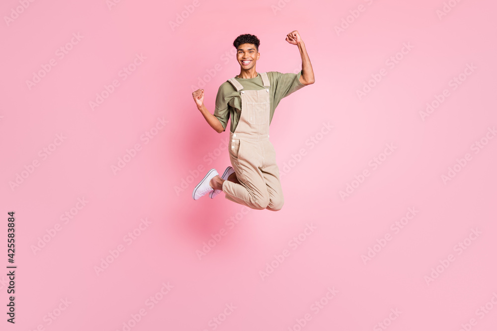 Full length body size photo of guy in overall jumping high gesturing like winner laughing isolated on pastel pink color background