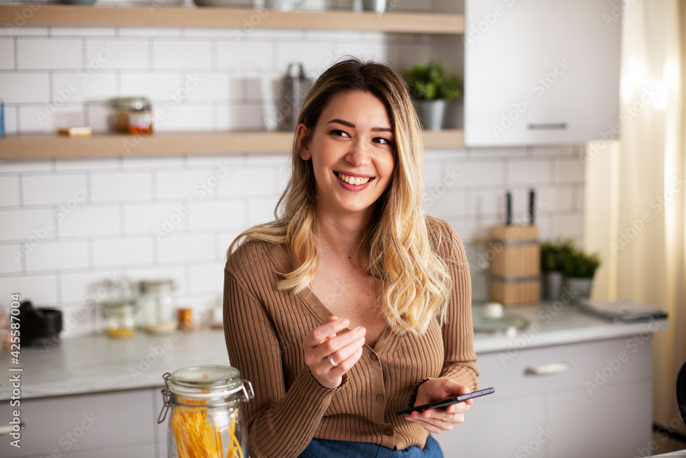 Young woman in kitchen. Beautiful woman using phone while making food. Young woman in kitchen. Beautiful woman using phone while making food.
