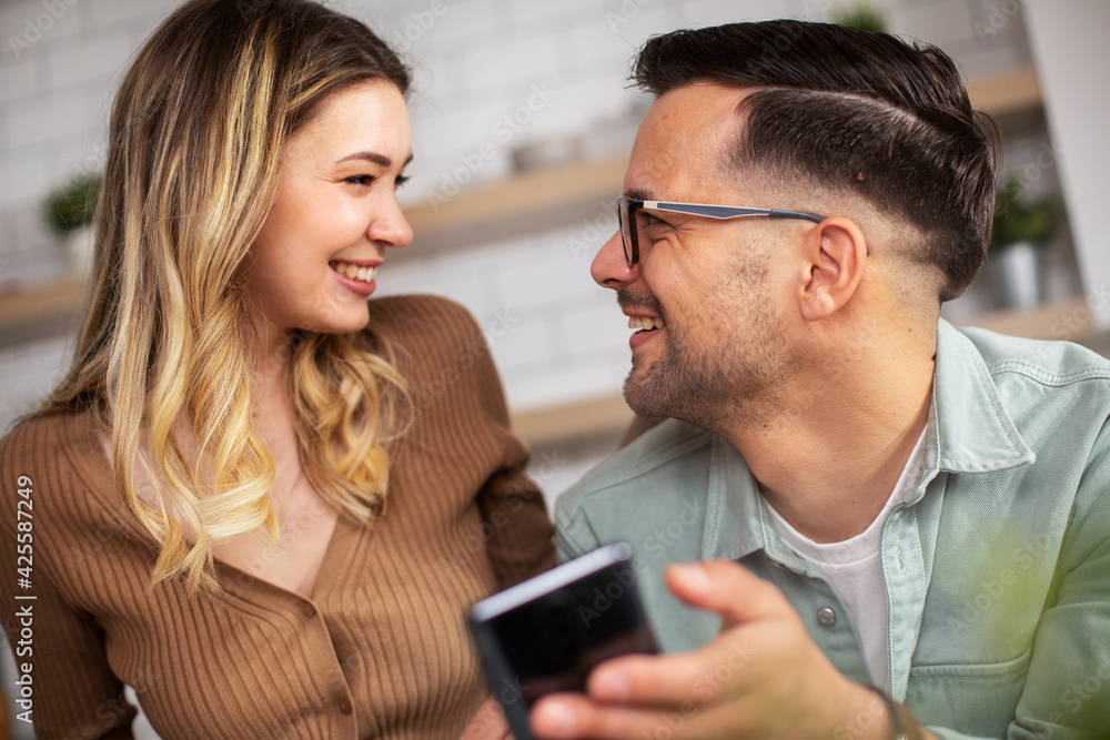 Loving couple in the kitchen. Happy smiling boyfriend and girlfriend using the phone, reading the news online Loving couple in the kitchen. Happy smiling boyfriend and girlfriend using the phone, reading the news online