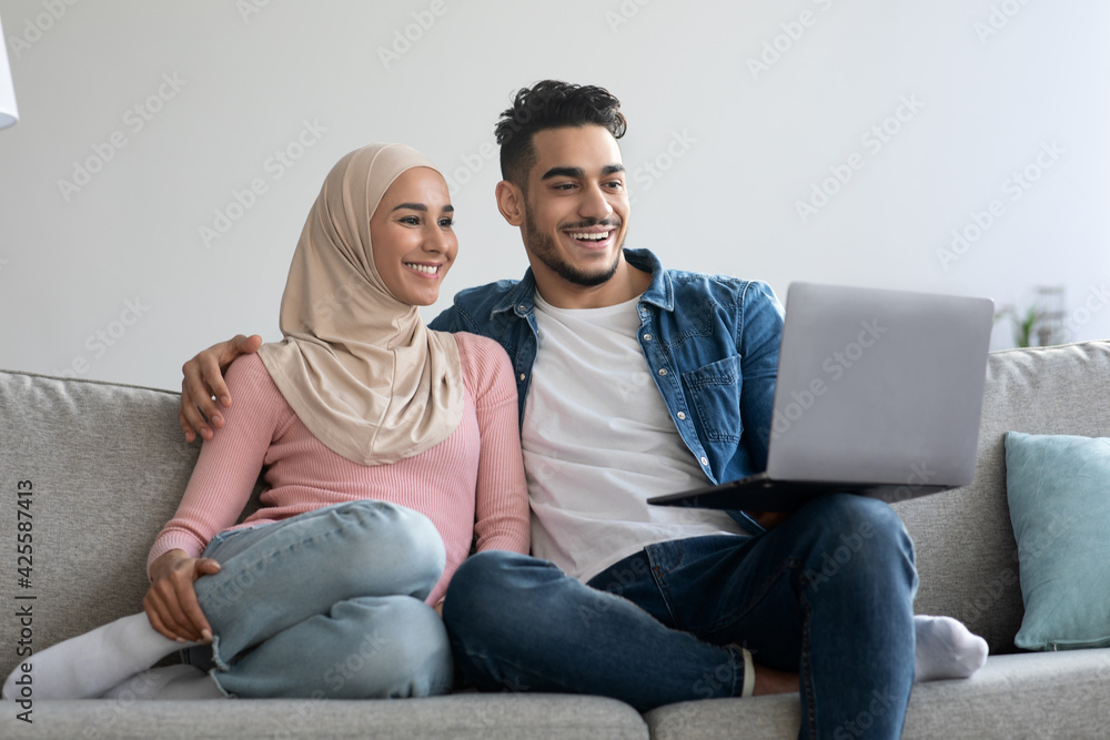 Happy young muslim family using laptop together at home