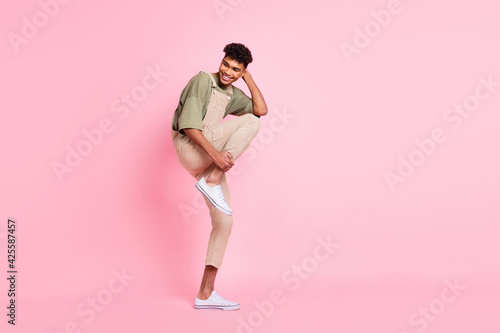 Photo of funny guy enjoy modern dance hands hold leg head wear beige overall sneakers isolated pink color background