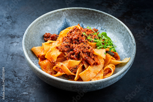 Modern style traditional Italian ragu alla bolognese sauce with papedelle pasta noodles and parmesan cheese served as close-up in a ceramic design bowl with copy space