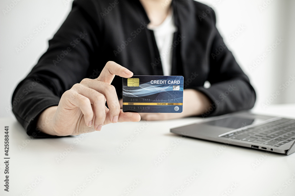 A business woman holds a credit card to make payments on the website where she is shopping online. Concept of using credit cards to pay for goods and services on online websites. A business woman holds a credit card to make payments on the website where she is shopping online. Concept of using credit cards to pay for goods and services on online websites.