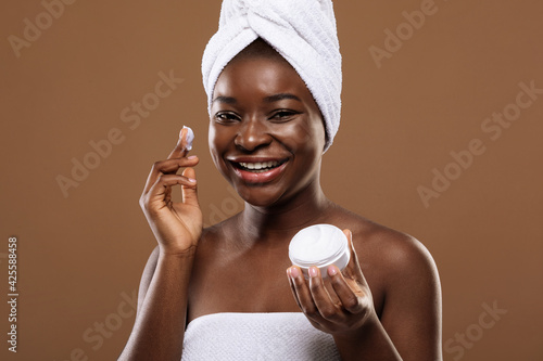 Skin Care Concept. Young Black Lady Applying Moisturizing Face Cream After Bath